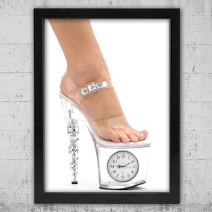 May include: A framed print featuring a clear platform high heel shoe with a clock face as the platform. The heel is embellished with silver-colored decorative elements. The shoe is worn by a person.