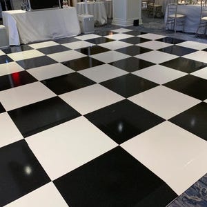 May include: A black and white checkered dance floor. The floor is made of glossy, square tiles arranged in an alternating pattern. The floor is clean and reflects light, creating a visually striking surface.
