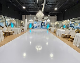 Può includere: Una sala eventi con un pavimento bianco lucido e un palco decorato con palloncini blu e bianchi, nuvole e un tema mongolfiera. Tavoli con tovaglie bianche e sedie dorate sono disposti ai lati del pavimento.