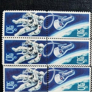 Puede incluir: Cuatro sellos postales estadounidenses vintage que muestran a un astronauta con un traje espacial flotando en el espacio con una nave espacial. Cada sello tiene un fondo azul y el texto "5c" impreso en blanco.