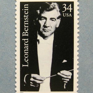 May include: A black and white postage stamp featuring a portrait of Leonard Bernstein, a conductor and composer. The stamp is from 2001 and has the text "Leonard Bernstein" and "34 USA" printed on it.