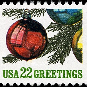 May include: A vintage postage stamp featuring Christmas ornaments and evergreen branches. The stamp has a red ornament in the foreground, with blue and yellow ornaments in the background. The text "USA 22 GREETINGS" is printed in green.
