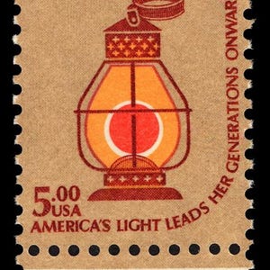 May include: A postage stamp featuring a stylized orange and red lantern with the text "AMERICA'S LIGHT LEADS HER GENERATIONS ONWARD." The stamp has a brown background and a face value of 5.00 USA.