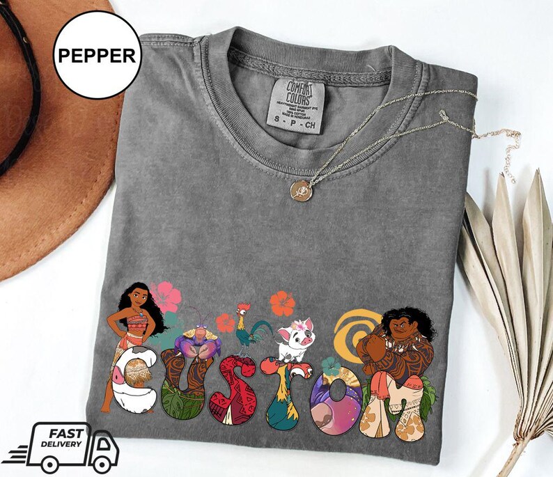 May include: Gray t-shirt with a custom design featuring characters from the animated film Moana. The design includes Moana, Maui, and other characters from the film. The text "CUSTOM" is spelled out using the characters.