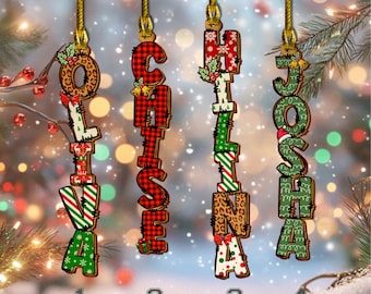 Puede incluir: Cuatro adornos navideños personalizados con los nombres Olivia, Chase, Christina y Josh. Cada adorno es una disposición vertical de letras con patrones festivos como cuadros escoceses y estampado de leopardo, suspendidos por cordones dorados.