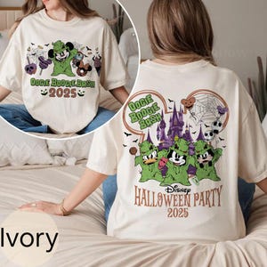 以下が含まれることがあります： ハロウィーンをテーマにしたアイボリー色のTシャツ。前面には、緑色のウギー・ブギーのキャラクターと「Oogie Boogie Bash 2025」の文字が描かれています。背面には、ディズニーのキャラクターと、お化け屋敷が描かれています。