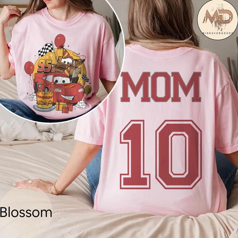 May include: Pink t-shirt with a cartoon image of a red race car with a birthday cake and presents on the front. The back of the shirt has the word "MOM" and the number "10" in red.