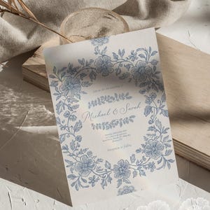 Op de afbeelding: Een huwelijksuitnodiging met een blauwe bloemenrand. De tekst luidt "Join us for the wedding of Michael & Sarah" en bevat de datum, tijd en locatie van de ceremonie en de receptie.