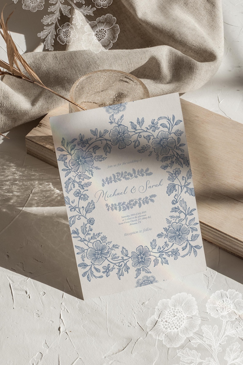 Op de afbeelding: Een huwelijksuitnodiging met een blauwe bloemenrand. De tekst luidt "Join us for the wedding of Michael & Sarah" en bevat de datum, tijd en locatie van de ceremonie en de receptie.