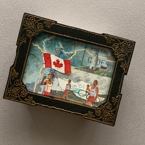 May include: A framed collage featuring a Canadian flag, a map, and a group of people rowing a boat. The frame is black with gold accents.