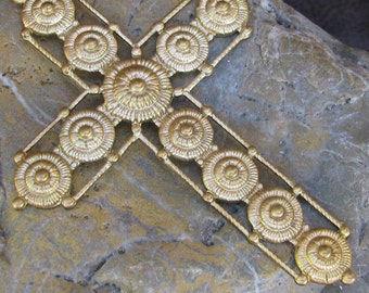 May include: A gold metal cross with a decorative design of concentric circles. The cross is made of a single piece of metal and has a smooth, polished finish.