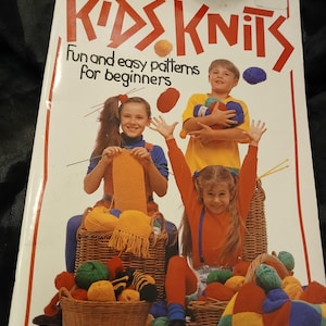 May include: A book cover titled "KIDS KNITS" with the text "Fun and easy patterns for beginners." The cover features illustrations of children with yarn and knitted items. Baskets of yarn in various colors are also shown.