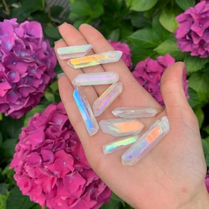 Könnte beinhalten: Eine Sammlung von regenbogenfarbenen, weißen Kristallspitzen mit einem regenbogenfarbenen Schimmer. Die Kristalle sind auf einer Hand angeordnet, wobei die Spitzen der Kristalle nach oben zeigen.