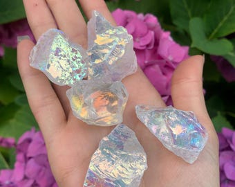 May include: A collection of five iridescent clear quartz crystals with rainbow reflections. The crystals are various shapes and sizes and are held in a hand.