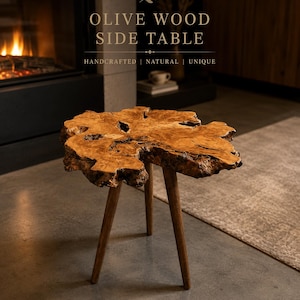 Puede incluir: Mesa auxiliar de madera de olivo con un borde natural y único. La mesa tiene una base de tres patas. El texto de la imagen dice: "OLIVE WOOD SIDE TABLE HANDCRAFTED | NATURAL | UNIQUE."