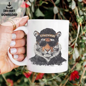May include: White ceramic mug featuring a graphic of a tiger wearing sunglasses and a black beanie with the word "CINCINNATI" on it.