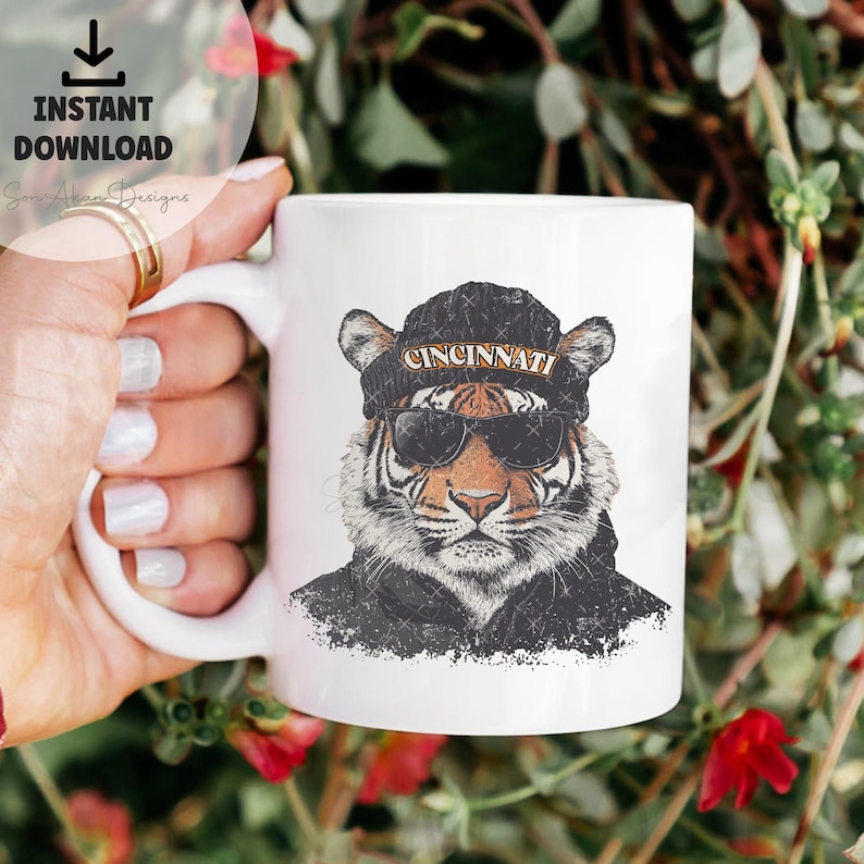 May include: White ceramic mug featuring a graphic of a tiger wearing sunglasses and a black beanie with the word "CINCINNATI" on it.
