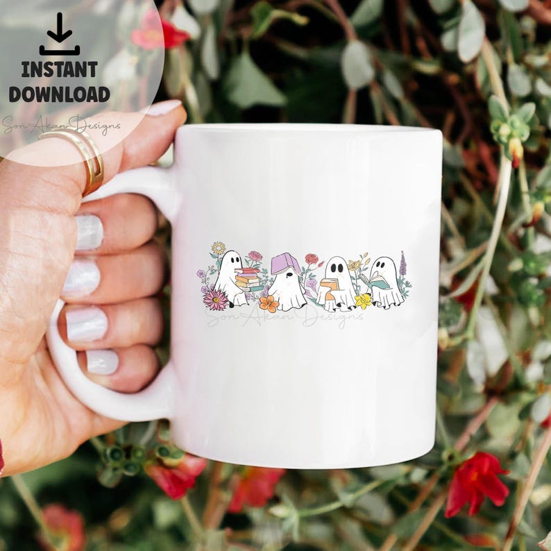 May include: White ceramic mug with a design of four ghosts reading books in a field of flowers. The text "Son Alkon Designs" is at the bottom of the mug.