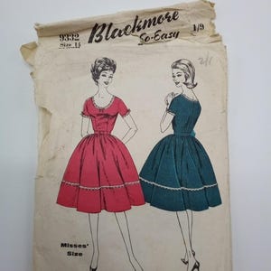 Op de afbeelding: Vintage naaipatroon voor een jurk, met twee vrouwen die de jurk in rood en blauw dragen. Het patroon is gelabeld "Blackmore So-Easy" en "9332 Maat 14".