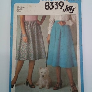May include: Simplicity sewing pattern number 8339 Jiffy for a skirt. The pattern is for sizes 14-16, medium, miss. The pattern shows two women wearing the skirt, one in a floral print and the other in a solid blue. A white dog is sitting in front of the women.