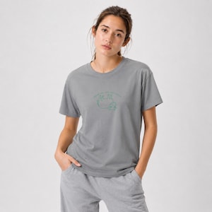 May include: A gray t-shirt with a green line drawing of a sloth and the text "I'm not slow, I'm just relaxed". The shirt is a crew neck and has short sleeves. The model is wearing gray sweatpants.