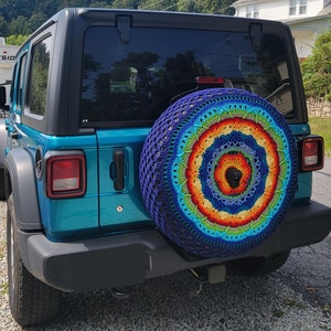 May include: A teal blue Jeep Wrangler with a colourful crocheted wheel cover. The cover features a rainbow mandala design with blue, green, yellow, orange, and red colours.