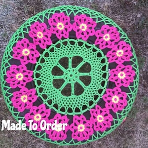 May include: A green crocheted doily with a pink crocheted border. The doily is circular and has a floral design. The doily is made to order.