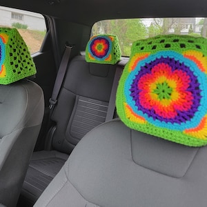 May include: Four crocheted headrest covers in a car. The covers are green with a multi-coloured flower design in the centre. The flowers are red, orange, yellow, green, blue, and purple.
