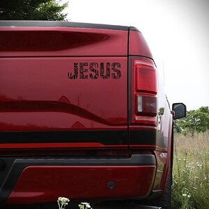 May include: A red pickup truck with a black decal on the back. The decal is a word cloud of positive words, including "hope", "peace", "faith", "love", "joy", "mercy", "truth", "freedom", "salvation", "strength", "purpose", "unity", and "redemption".