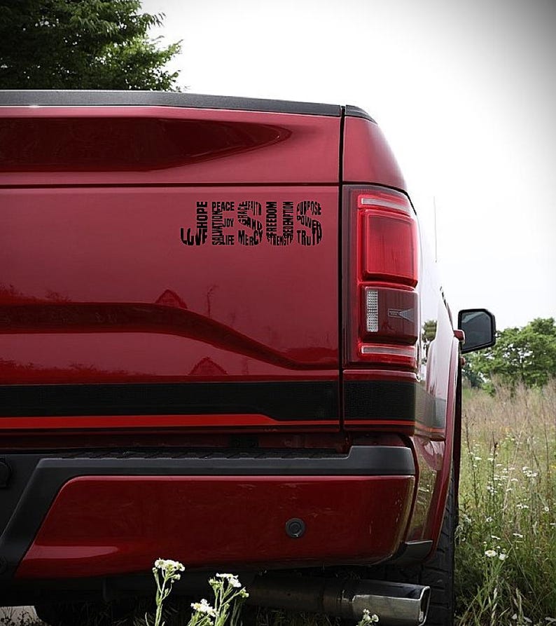 May include: A red pickup truck with a black decal on the back. The decal is a word cloud of positive words, including "hope", "peace", "faith", "love", "joy", "mercy", "truth", "freedom", "salvation", "strength", "purpose", "unity", and "redemption".