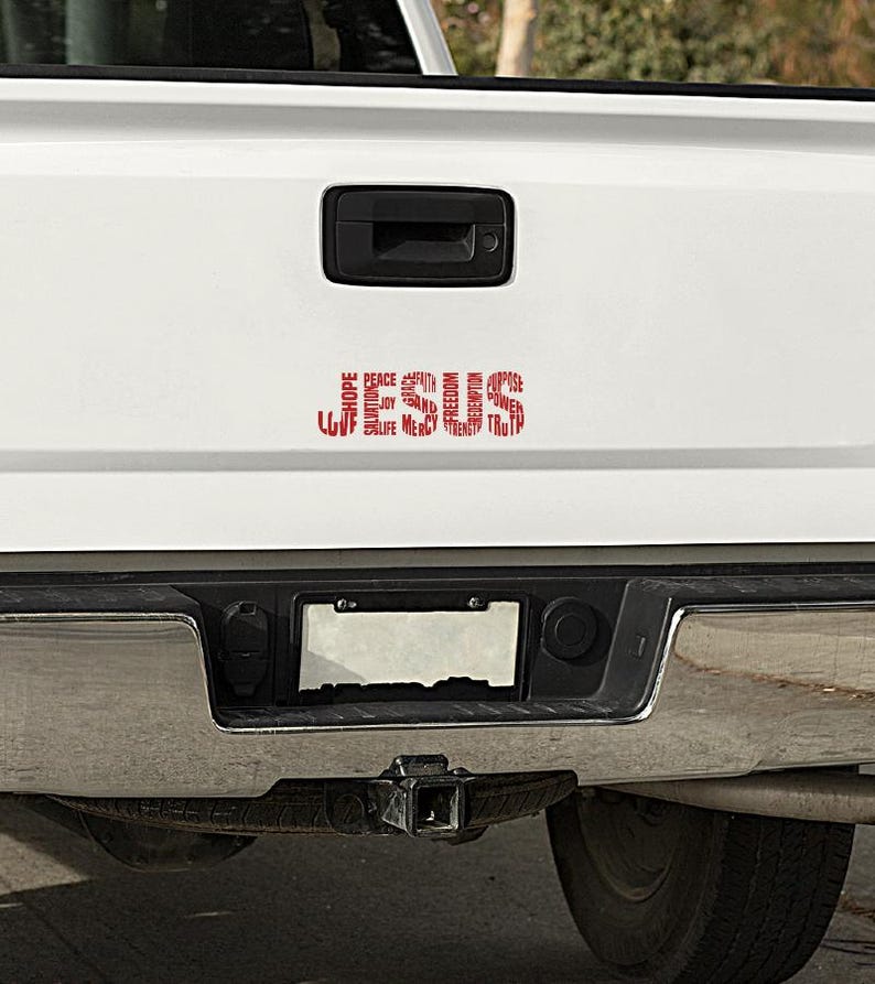May include: A white pickup truck with a red word art decal on the tailgate. The decal is a circle of words including "love", "life", "joy", "peace", "hope", "faith", "mercy", "truth", "strength", "freedom", "redemption", "salvation", "purpose", and "power".