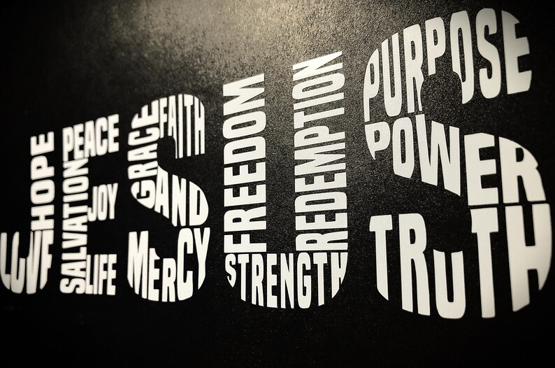 May include: Black background with white text spelling out the word "JESUS" in large letters.  The letters are made up of smaller words, including "love", "hope", "peace", "joy", "salvation", "life", "grace", "faith", "mercy", "and", "freedom", "redemption", "strength", "purpose", "power", and "truth".