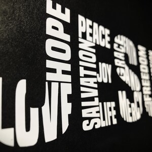 May include: Black background with white text spelling out the words "LOVE", "HOPE", "SALVATION", "PEACE", "JOY", "LIFE", "GRACE", "MERCY", "AND", "FREEDOM", "JESUS".