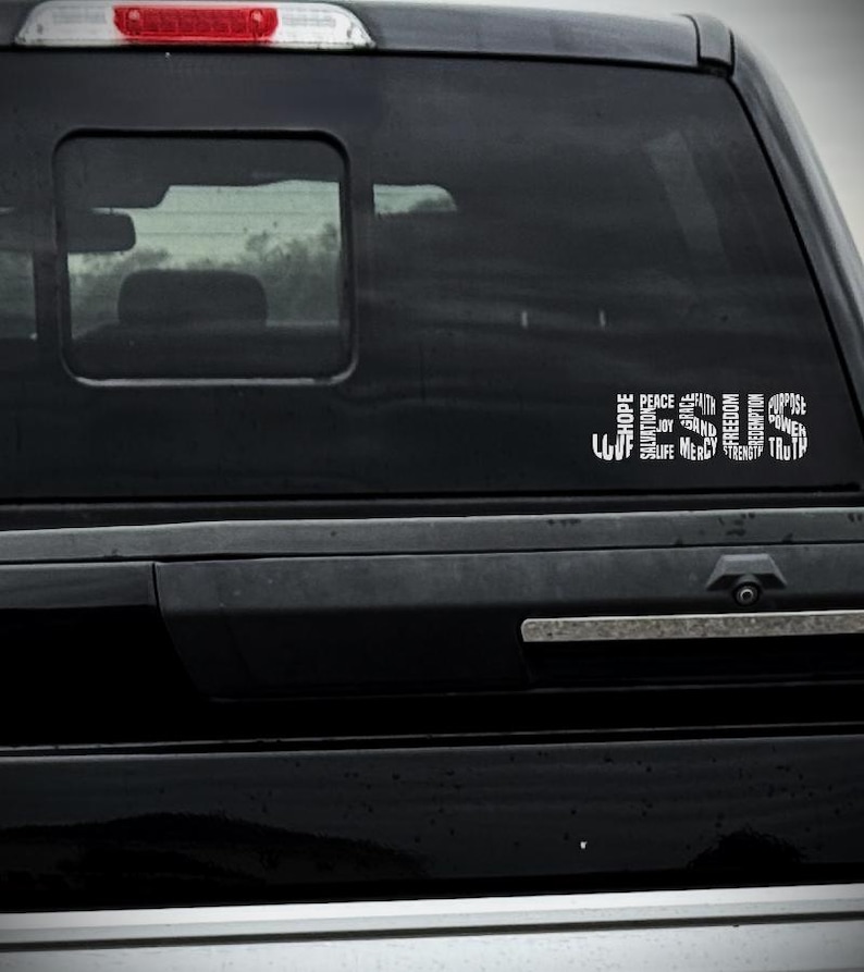 May include: A black truck with a white vinyl decal on the rear window. The decal is a word cloud of positive words, including "love", "hope", "peace", "faith", "joy", "strength", "mercy", "truth", "freedom", "purpose", and "salvation".