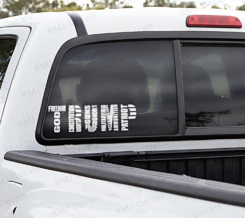 May include: A white pickup truck with a black window decal that reads "TRUMP" in large letters. The decal is made up of smaller words, including "God, Constitution, Rights, Guns, Bible, Military, Honor, Prof, Ammo, Patriot, Life".