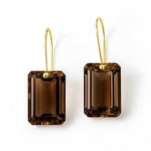 May include: A pair of rectangular, faceted, smoky quartz earrings with gold-coloured hooks. The earrings have a warm brown hue and are set against a white background. The gold hooks are simple and elegant.