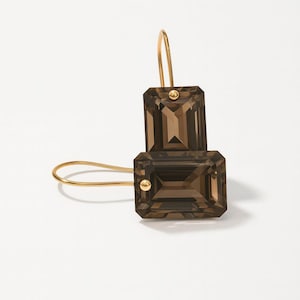May include: A pair of gold-tone earrings featuring rectangular, smoky brown gemstones. The earrings have a hook closure and a small gold accent on each gemstone. The gemstones are faceted, catching the light.