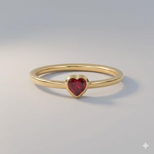 May include: A gold ring featuring a heart-shaped, red gemstone. The ring has a slender, polished band, and the gemstone is set in a bezel. This ring is a romantic piece of jewellery.