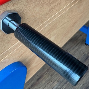 Peut inclure: Une poignée de baby-foot noire avec une prise texturée. La poignée est fixée à une tige en métal argenté.