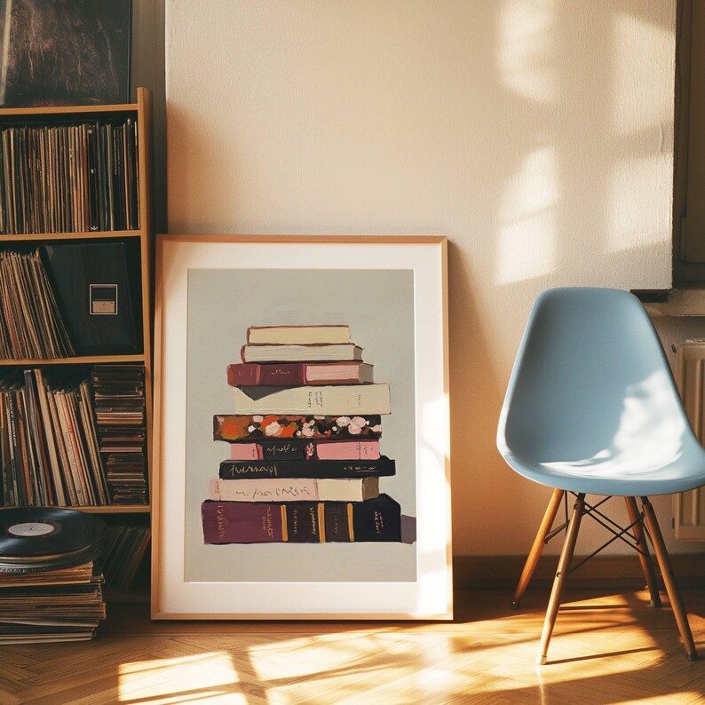 May include: A framed print of a stack of books with different coloured covers on a light grey background. The books are stacked in a pile, with the top book being a light beige colour. The other books are a mix of dark red, pink, and black.