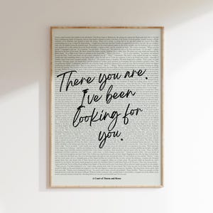 May include: A framed print with a light wood-colored frame. The print features a background of printed text with the words "There you are. I've been looking for you" in a cursive font. The text "A Court of Thorns and Roses" is at the bottom.