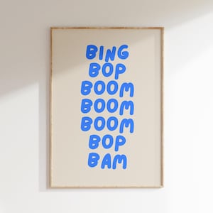 Może przedstawiać: Oprawiony plakat z napisem "BING BOP BOOM BOOM BOOM BOP BAM" w niebieskich, zaokrąglonych literach. Tekst jest wyśrodkowany na beżowym tle, w cienkiej, jasnobrązowej drewnianej ramie. Grafika jest zawieszona na białej ścianie.