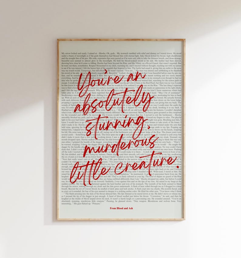May include: A framed print with a cream-colored background filled with small text. Bold, red cursive text reads "You're an absolutely stunning, murderous little creature." The bottom of the print reads "From Blood and Ash."