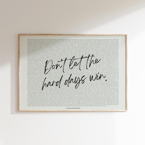 Puede incluir: Una impresi&oacute;n enmarcada con un fondo claro lleno de texto peque&ntilde;o. Las palabras "Don't let the hard days win" est&aacute;n escritas en una fuente cursiva y en negrita en el centro. La parte inferior de la impresi&oacute;n dice "A Court of Mist and Fury".