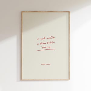 Op de afbeelding: Een ingelijste kunstafdruk met een crèmekleurige achtergrond. Rode handgeschreven tekst in Cyrillisch en Engels luidt "I love you". De woorden zijn onderstreept met een rode lijn. De tekst "HEATED RIVALRY" staat onderaan afgedrukt.