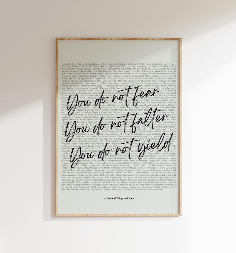 May include: Framed art print with a light beige border. The artwork features a background of printed text with the phrases "You do not fear", "You do not falter", and "You do not yield" in elegant script. The title "A Court of Wings and Ruin" is at the bottom.
