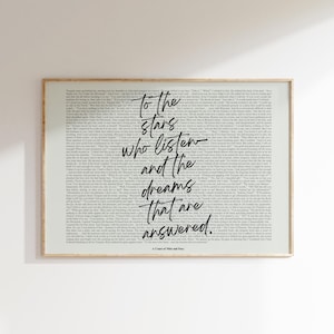 May include: A framed print with a light background filled with small text. The center features the quote "To the stars who listen and the dreams that are answered" in black script. The frame is a light brown color.