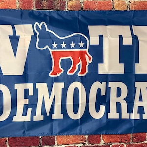 May include: A blue political flag with white text that reads "Vote Democrat". A white donkey with red and blue stars is in the centre of the flag.