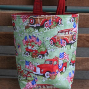 May include: Red, white, and blue tote bag with a green background and a pattern of vintage cars and American flags. The bag has red handles.