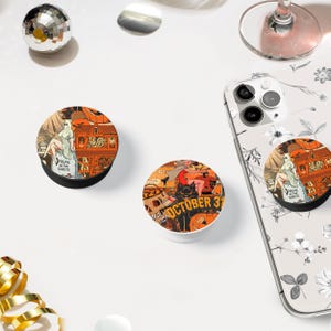 Könnte beinhalten: Drei Halloween-Telefon-Griffe mit verschiedenen Designs. Ein Griff zeigt ein Spukhaus mit einem Geist, ein anderer einen Totenkopf und gekreuzte Knochen und der dritte eine Hexe auf einem Besen. Alle drei Griffe sind orange und schwarz.